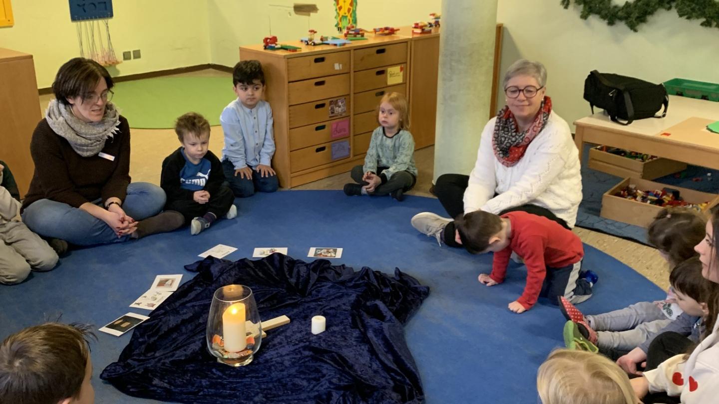In einem Sitzkreis sitzen mehrere Kinder, zwei Erwachsene sitzen dabei.